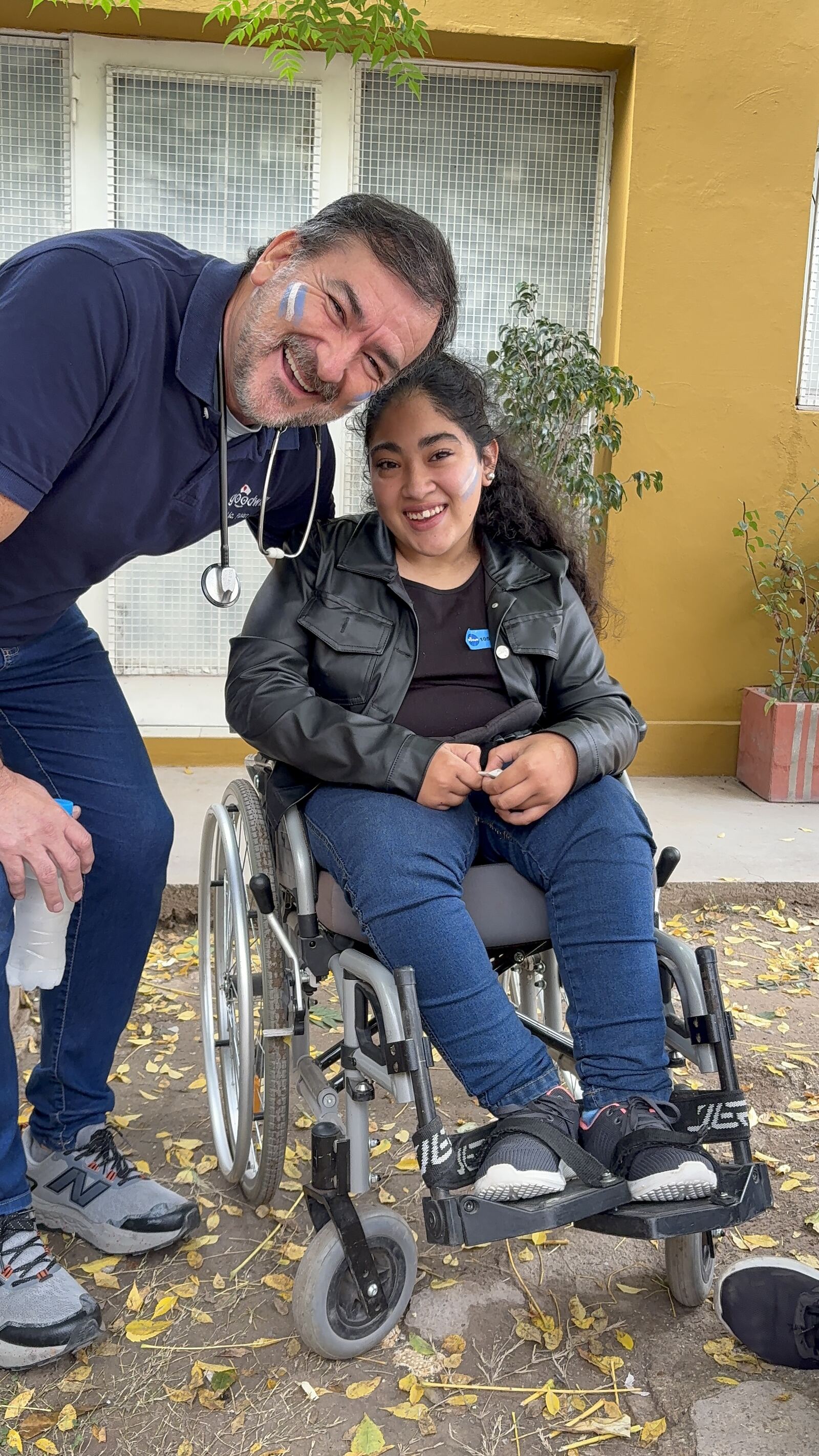 Un médico agachado junto a una joven en silla de ruedas, los dos sonriendo.